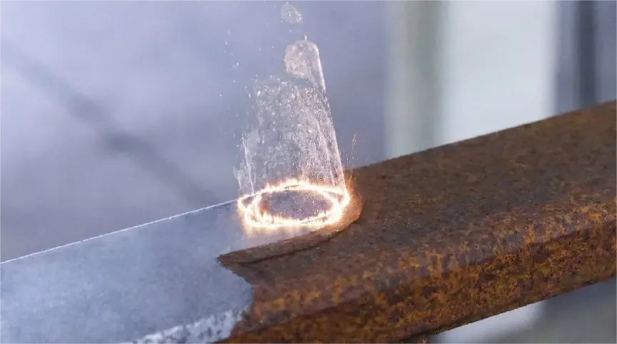 Close-up of round steel bar during laser rust removal showing clean metal emerging